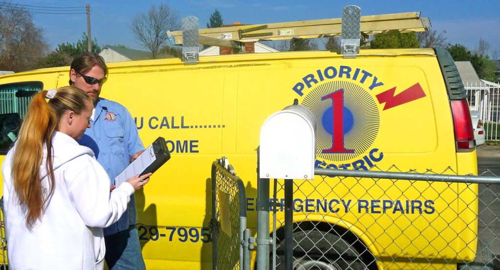 A Priority 1 Electric technician going over the work with a customer beside the company van.
